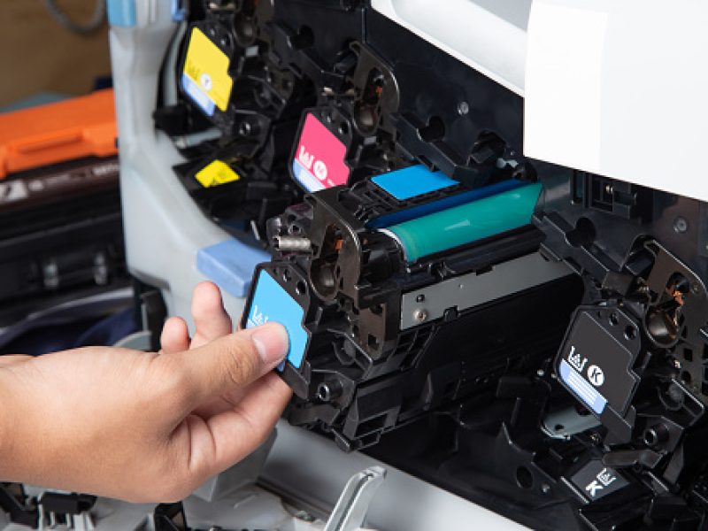 Business man or technician is checking and changing the printer equipment cartridges tone of laser jet multi function printer in the office. Close-up shot of CMYK ink cartridges for laser printer.